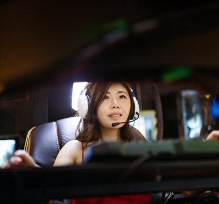 a woman playing video games, like Genshin Impact on the PC, wearing headphones