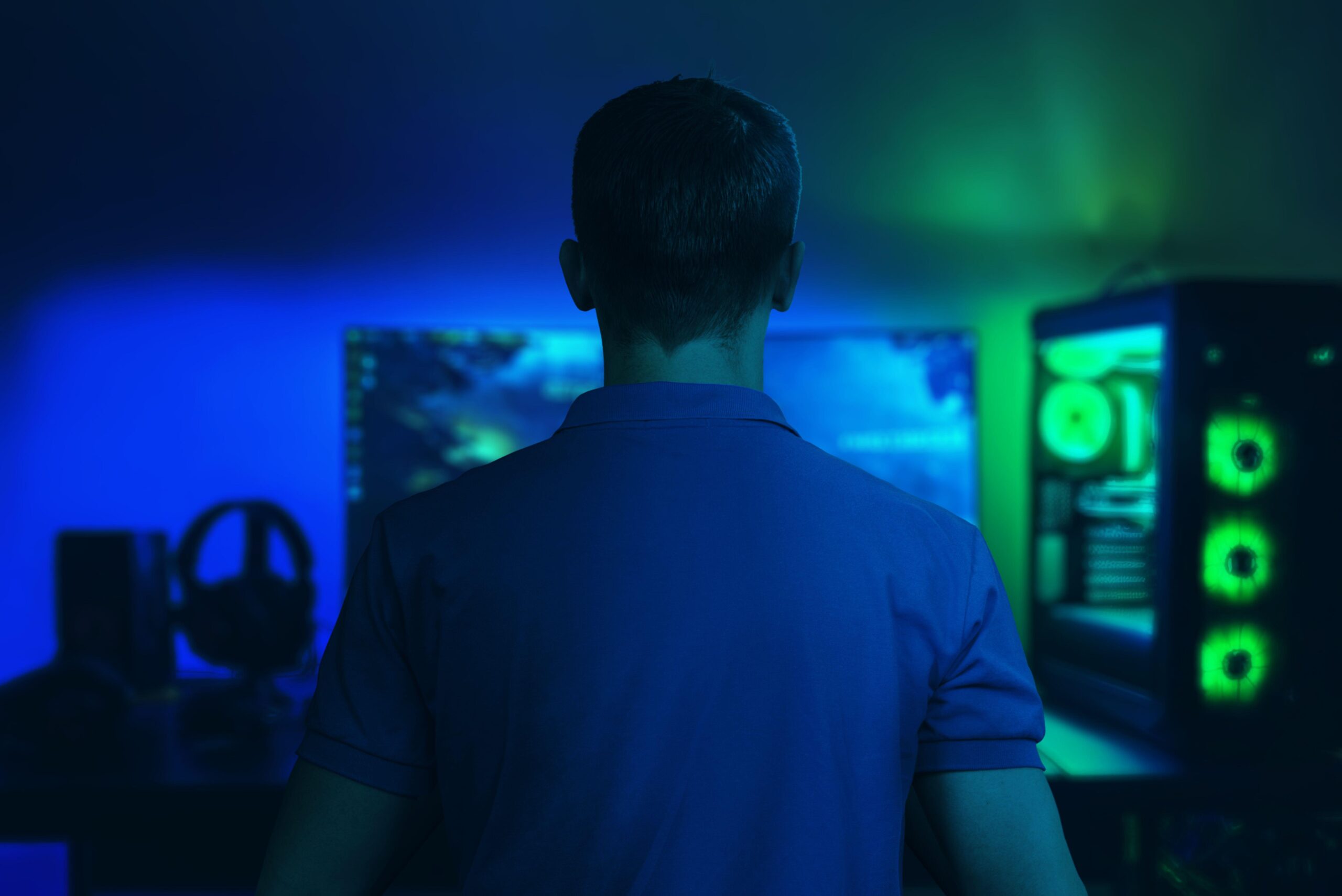 a man sitting in a dark room playing The Precinct on his PC that glows blue and green