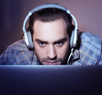 a man leaning into the monitor with a headset on while playing the intense roguelite The King is Watching